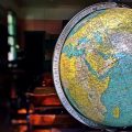 geography 地理知识编辑在灯下翻阅地图册与气候统计资料，桌面摊开多张等高线图，暖色台灯光线营造专注审校氛围